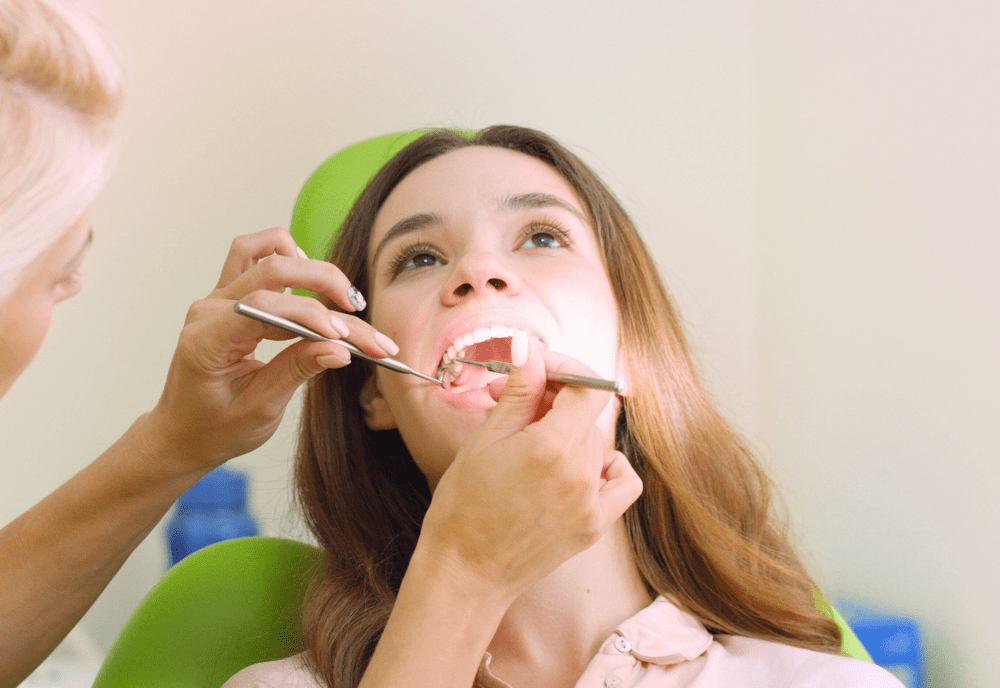Hands using dental tools in woman's mouth.