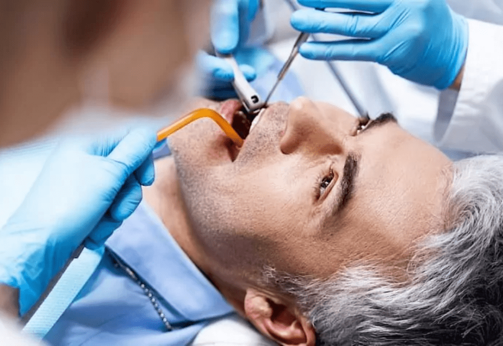 Gloved hands using dental tools in male patient's mouth.