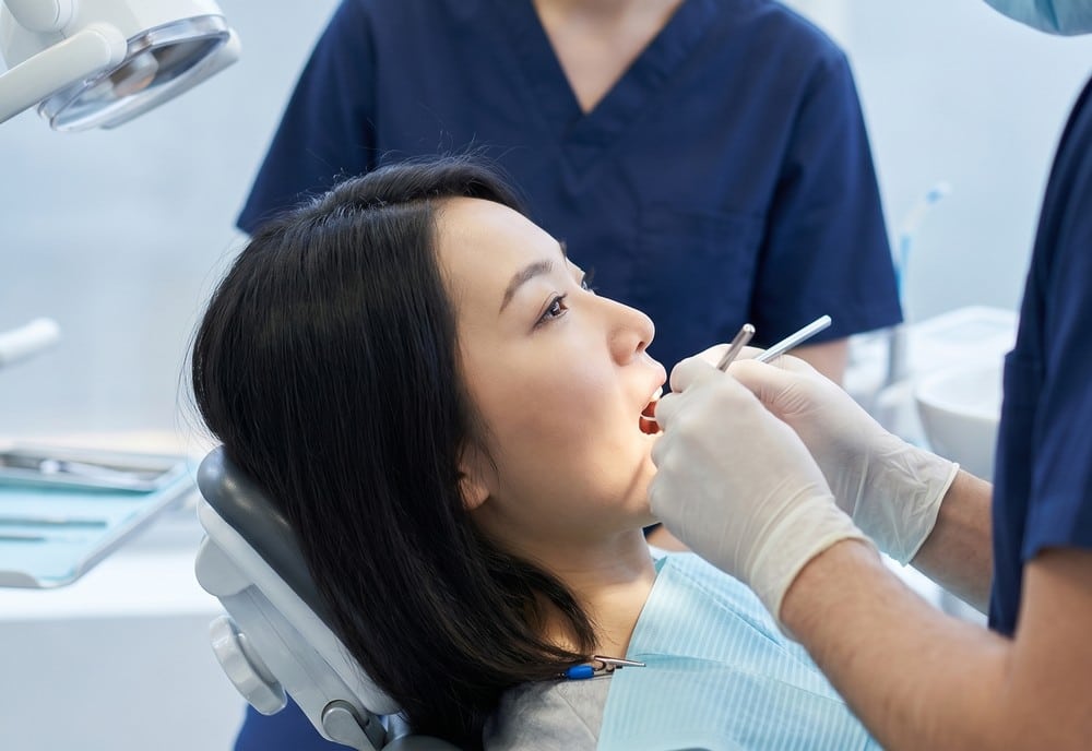 Dentist using dentals tools in female patient's mouth.